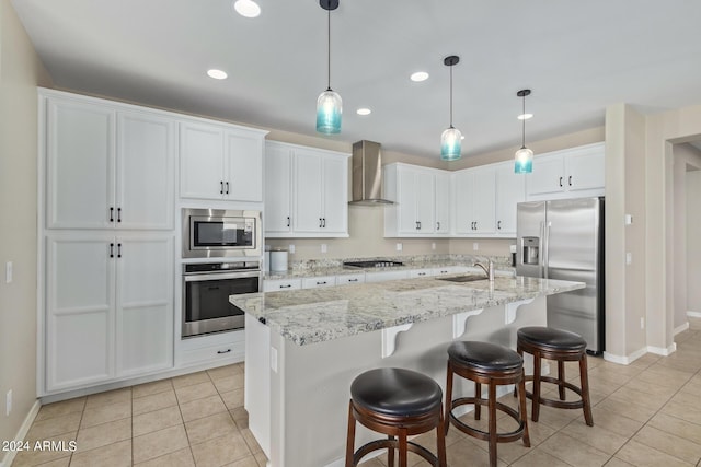 kitchen with light tile patterned floors, white cabinetry, an island with sink, stainless steel appliances, and wall chimney range hood