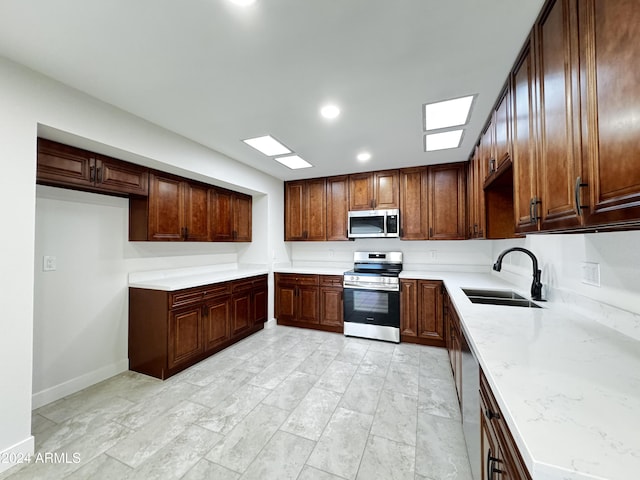 kitchen with light stone counters, sink, stainless steel appliances, and a skylight