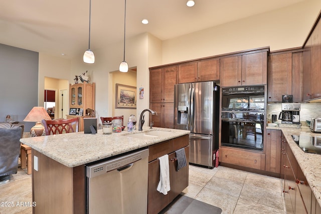 kitchen featuring pendant lighting, sink, black appliances, light stone countertops, and a center island with sink