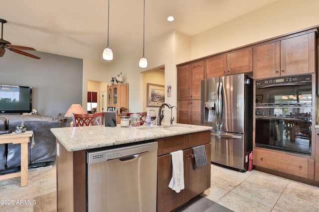 kitchen with sink, appliances with stainless steel finishes, pendant lighting, light stone countertops, and a kitchen island with sink