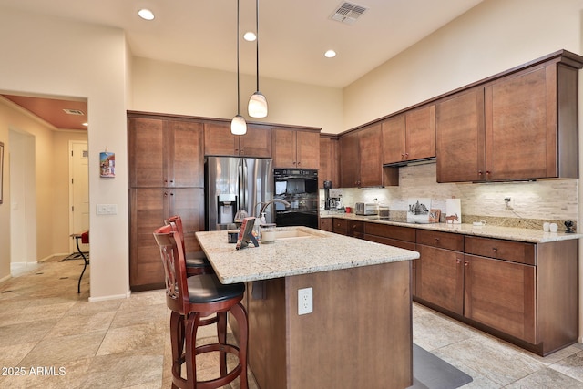 kitchen with sink, a kitchen island with sink, black appliances, light stone countertops, and decorative light fixtures