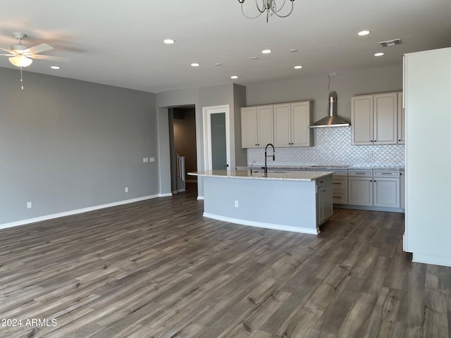 kitchen with sink, wall chimney exhaust hood, tasteful backsplash, dark hardwood / wood-style floors, and a kitchen island with sink