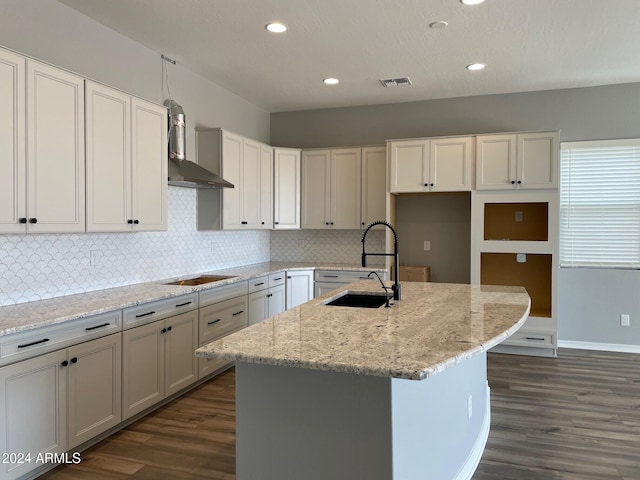 kitchen featuring a center island with sink, light stone counters, sink, and dark wood-type flooring