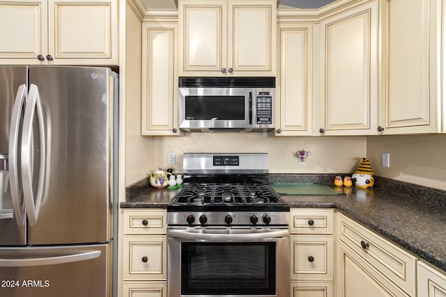 kitchen featuring cream cabinetry, appliances with stainless steel finishes, and dark stone counters