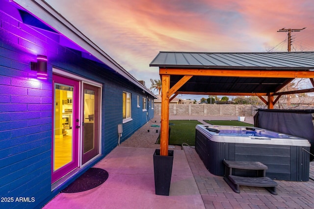 patio terrace at dusk with a hot tub, a fenced backyard, and a gazebo