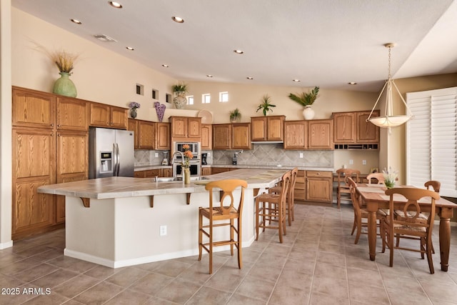 kitchen featuring light tile patterned floors, backsplash, appliances with stainless steel finishes, and brown cabinetry