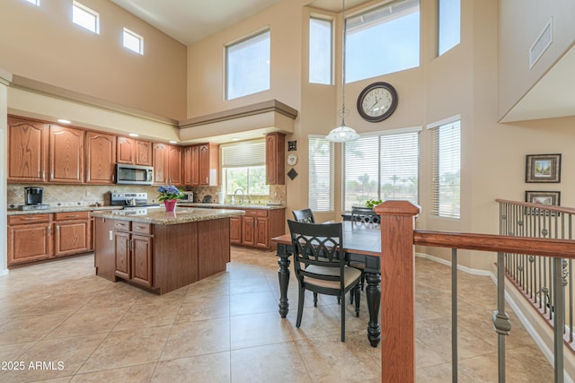 21841 N Ingram Ct, Maricopa, AZ 85138 - kitchen featuring appliances with stainless steel finishes, a center island, brown cabinets, tasteful backsplash, and a towering ceiling