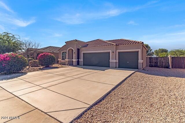 mediterranean / spanish-style house with stucco siding, fence, a tile roof, driveway, and an attached garage