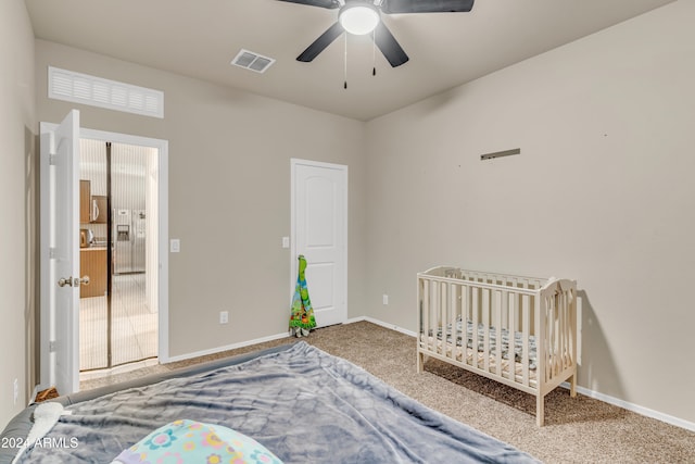 bedroom featuring a nursery area, ceiling fan, and carpet