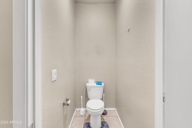 bathroom with baseboards, toilet, tile patterned flooring, and a textured wall