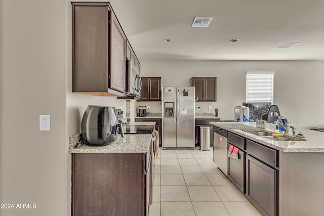 kitchen with light tile patterned floors, a kitchen island with sink, appliances with stainless steel finishes, dark brown cabinets, and sink