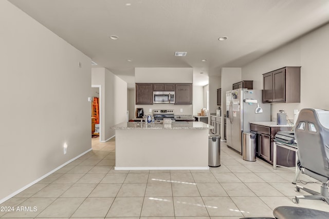 kitchen with appliances with stainless steel finishes, visible vents, dark brown cabinetry, light stone countertops, and an island with sink