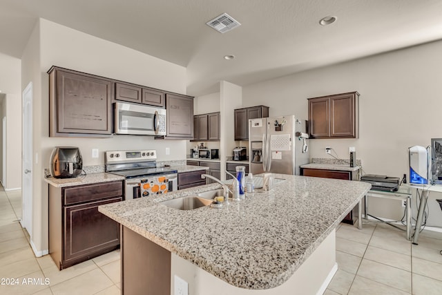 kitchen with sink, light tile patterned floors, dark brown cabinets, a center island with sink, and appliances with stainless steel finishes