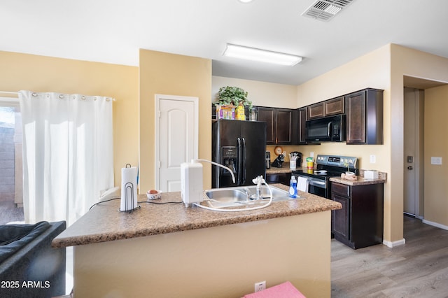 kitchen featuring visible vents, dark brown cabinetry, light wood-style floors, black appliances, and a sink