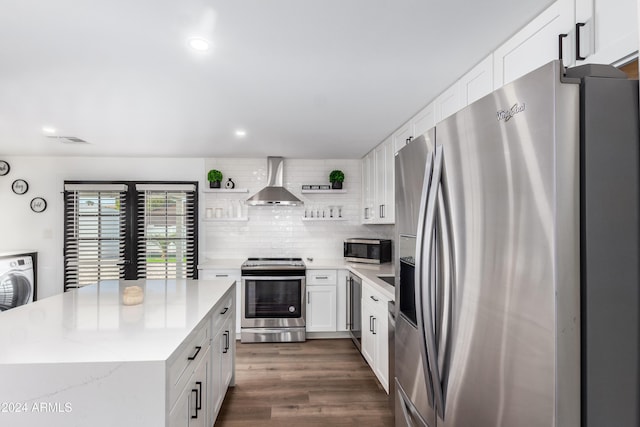 kitchen with appliances with stainless steel finishes, wall chimney exhaust hood, dark wood-type flooring, washer / dryer, and white cabinetry