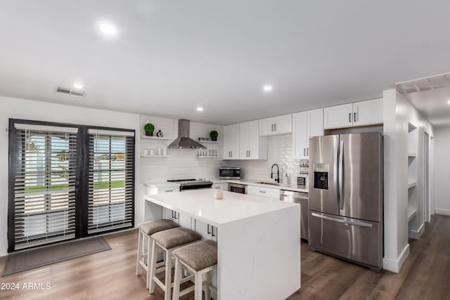 kitchen with a kitchen bar, appliances with stainless steel finishes, a kitchen island, wall chimney range hood, and white cabinetry