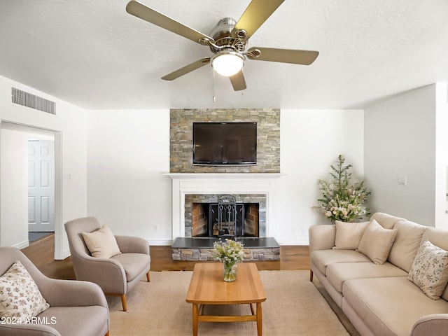 living room with a stone fireplace, hardwood / wood-style flooring, and ceiling fan