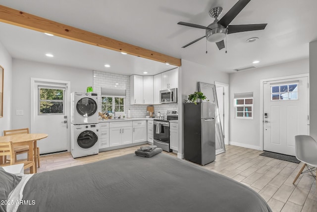 kitchen with beam ceiling, white cabinetry, stainless steel appliances, decorative backsplash, and stacked washer and clothes dryer