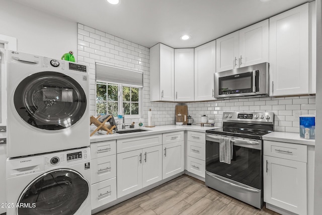 kitchen with white cabinets, light hardwood / wood-style flooring, appliances with stainless steel finishes, and stacked washer and clothes dryer