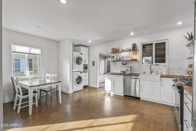 kitchen with wood counters, stainless steel appliances, sink, stacked washer and clothes dryer, and white cabinets