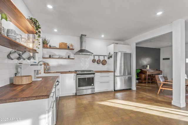 kitchen featuring butcher block counters, white cabinetry, wall chimney exhaust hood, stainless steel appliances, and tasteful backsplash