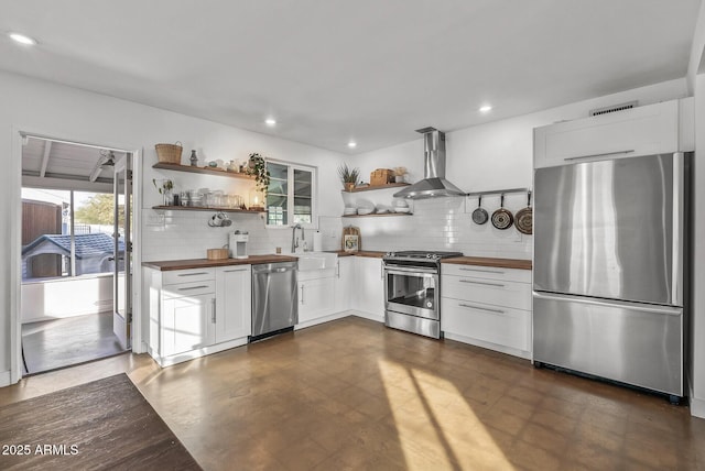 kitchen featuring decorative backsplash, appliances with stainless steel finishes, wall chimney exhaust hood, sink, and white cabinets