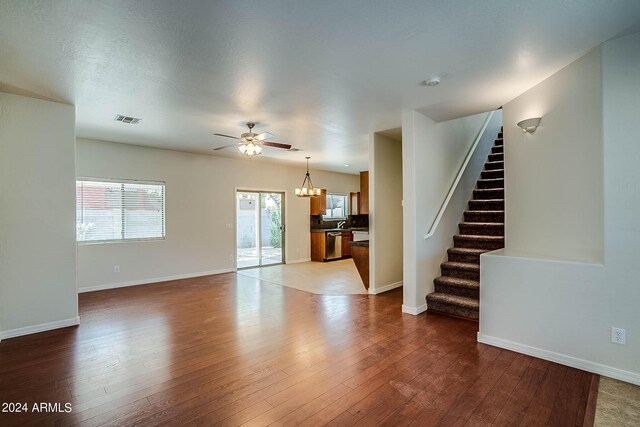 unfurnished living room with ceiling fan with notable chandelier, a textured ceiling, and wood-type flooring