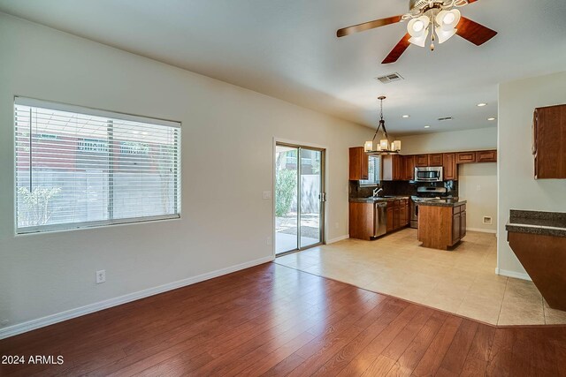 kitchen with ceiling fan with notable chandelier, appliances with stainless steel finishes, light hardwood / wood-style floors, hanging light fixtures, and sink