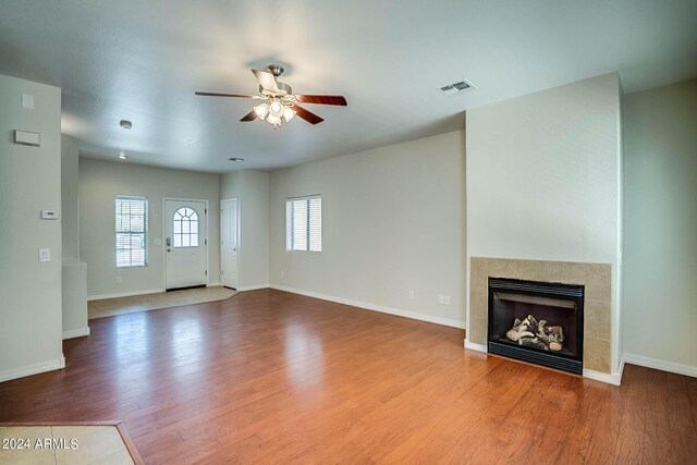 unfurnished living room with a tiled fireplace, hardwood / wood-style floors, and ceiling fan