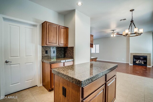 kitchen with hanging light fixtures, a fireplace, a center island, ceiling fan with notable chandelier, and light hardwood / wood-style floors