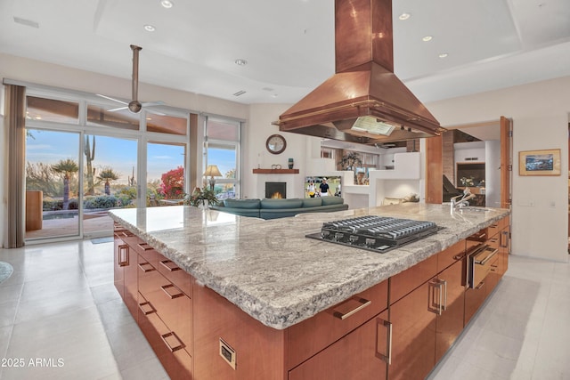 kitchen with a spacious island, ceiling fan, light stone countertops, island exhaust hood, and black gas stovetop