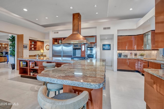 kitchen with light stone counters, island range hood, a kitchen breakfast bar, stainless steel appliances, and decorative backsplash