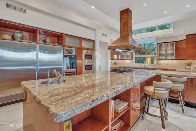 kitchen featuring island range hood, sink, decorative backsplash, stainless steel appliances, and light stone countertops