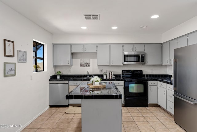 kitchen with tile counters, stainless steel appliances, gray cabinets, and a kitchen island