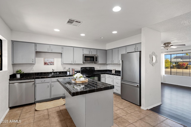 kitchen with gray cabinets, ceiling fan, appliances with stainless steel finishes, a kitchen island, and tile countertops