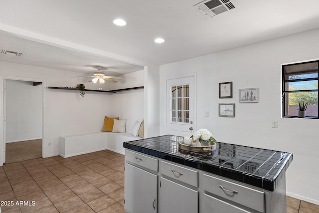 kitchen with light tile patterned flooring, ceiling fan, tile countertops, and a center island