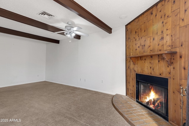 unfurnished living room featuring ceiling fan, carpet, a fireplace, a textured ceiling, and beamed ceiling