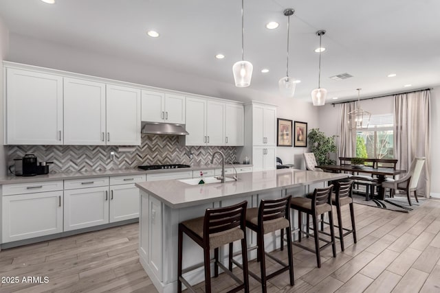 kitchen with pendant lighting, stainless steel gas stovetop, an island with sink, white cabinets, and a kitchen bar