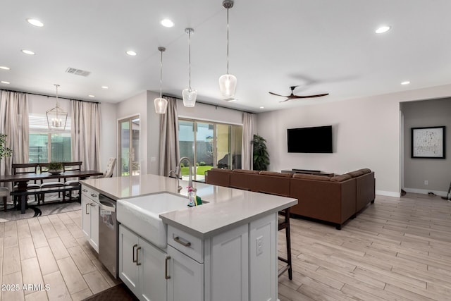 kitchen featuring an island with sink, sink, white cabinets, hanging light fixtures, and light hardwood / wood-style flooring