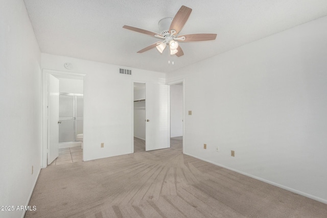 unfurnished bedroom with a walk in closet, a closet, light colored carpet, ceiling fan, and connected bathroom