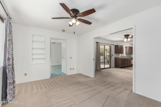 unfurnished room featuring ceiling fan, light colored carpet, a textured ceiling, and built in shelves