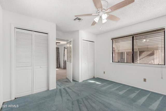 unfurnished bedroom with multiple closets, a textured ceiling, carpet, and ceiling fan