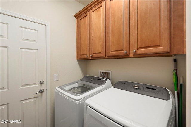 clothes washing area with washing machine and clothes dryer and cabinets