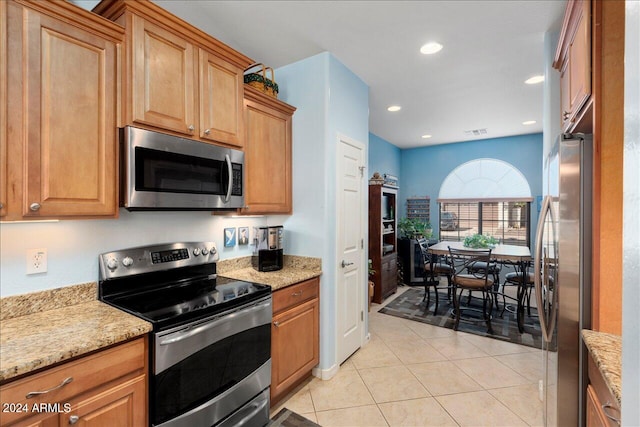 kitchen with stainless steel appliances, light tile patterned flooring, and light stone counters