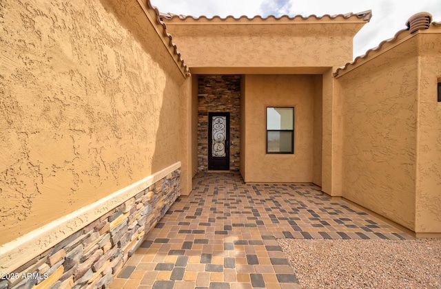 view of exterior entry with stone siding, a tiled roof, and stucco siding