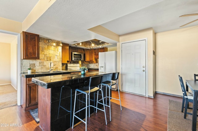 kitchen with a breakfast bar, a center island, backsplash, dark wood-type flooring, and white fridge with ice dispenser