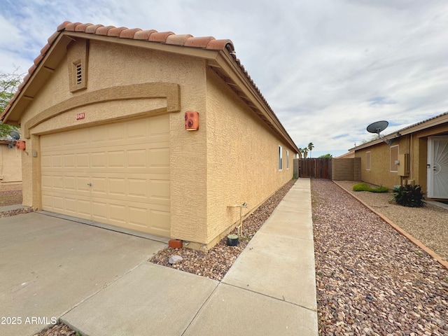 view of side of property featuring a tiled roof, fence, concrete driveway, and stucco siding