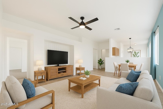 living room with light tile patterned floors, visible vents, ceiling fan with notable chandelier, and baseboards