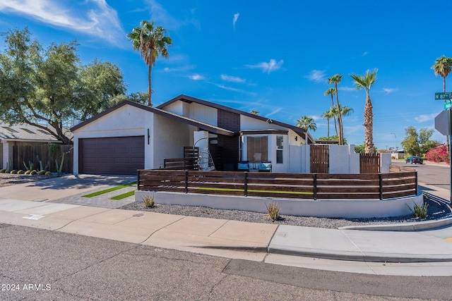 mid-century inspired home with a garage, concrete driveway, a fenced front yard, and stucco siding