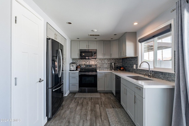 kitchen featuring wood finished floors, a sink, gray cabinets, backsplash, and black appliances